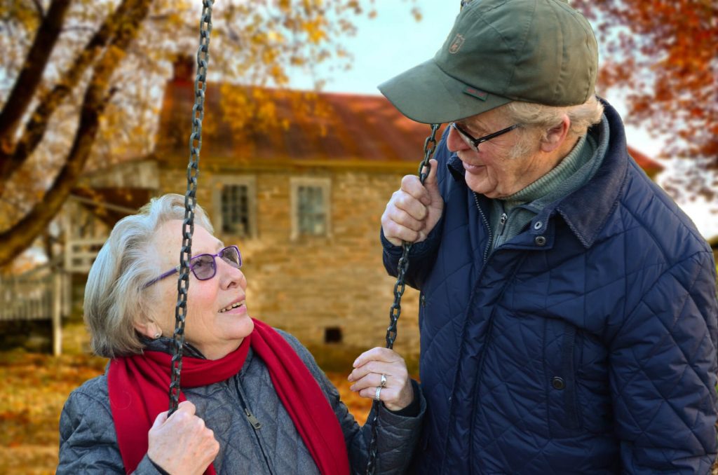An elderly couple shares a tender moment on a swing outdoors.